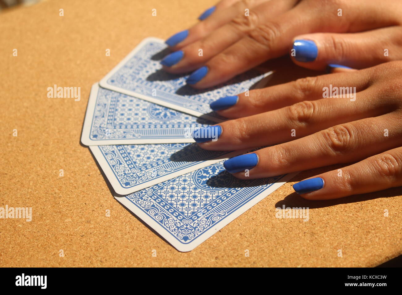 Mani femminili con le unghie blu diffusione pack di blu carte da gioco sul tavolo di legno. Foto Stock