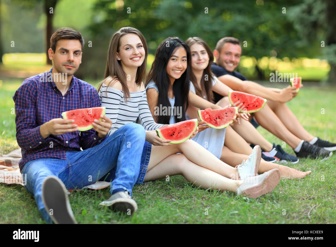 Cinque sorridente uomini e donne con fette di cocomero all'esterno. giovani amici studenti divertendosi al picnic con frutta succosa sulla giornata calda. Le persone felici Foto Stock