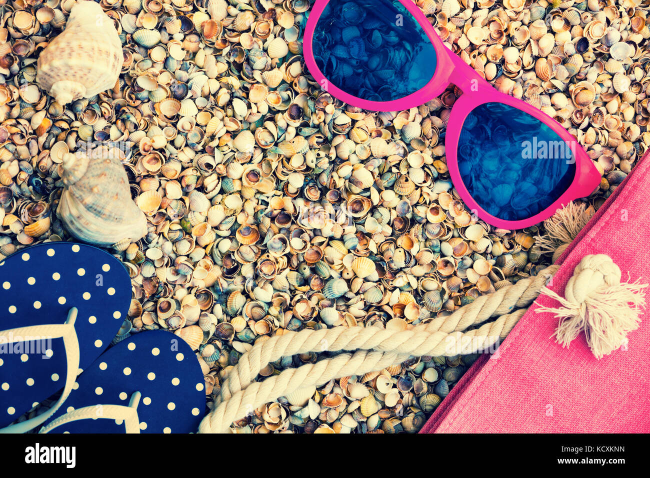 Scena di spiaggia. Accessori donna. Occhiali da sole, flip flop sandali e borsa da spiaggia sdraiato sul mare coquina gusci Foto Stock