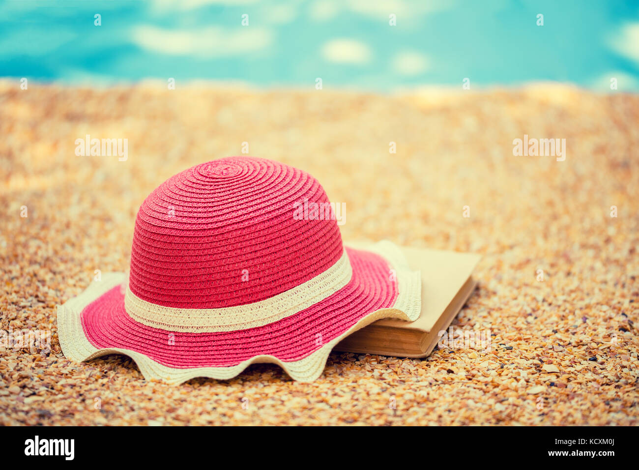 Scena di spiaggia. Sun cappello di paglia e prenota giacente sul mare coquina conchiglie sulla spiaggia Foto Stock