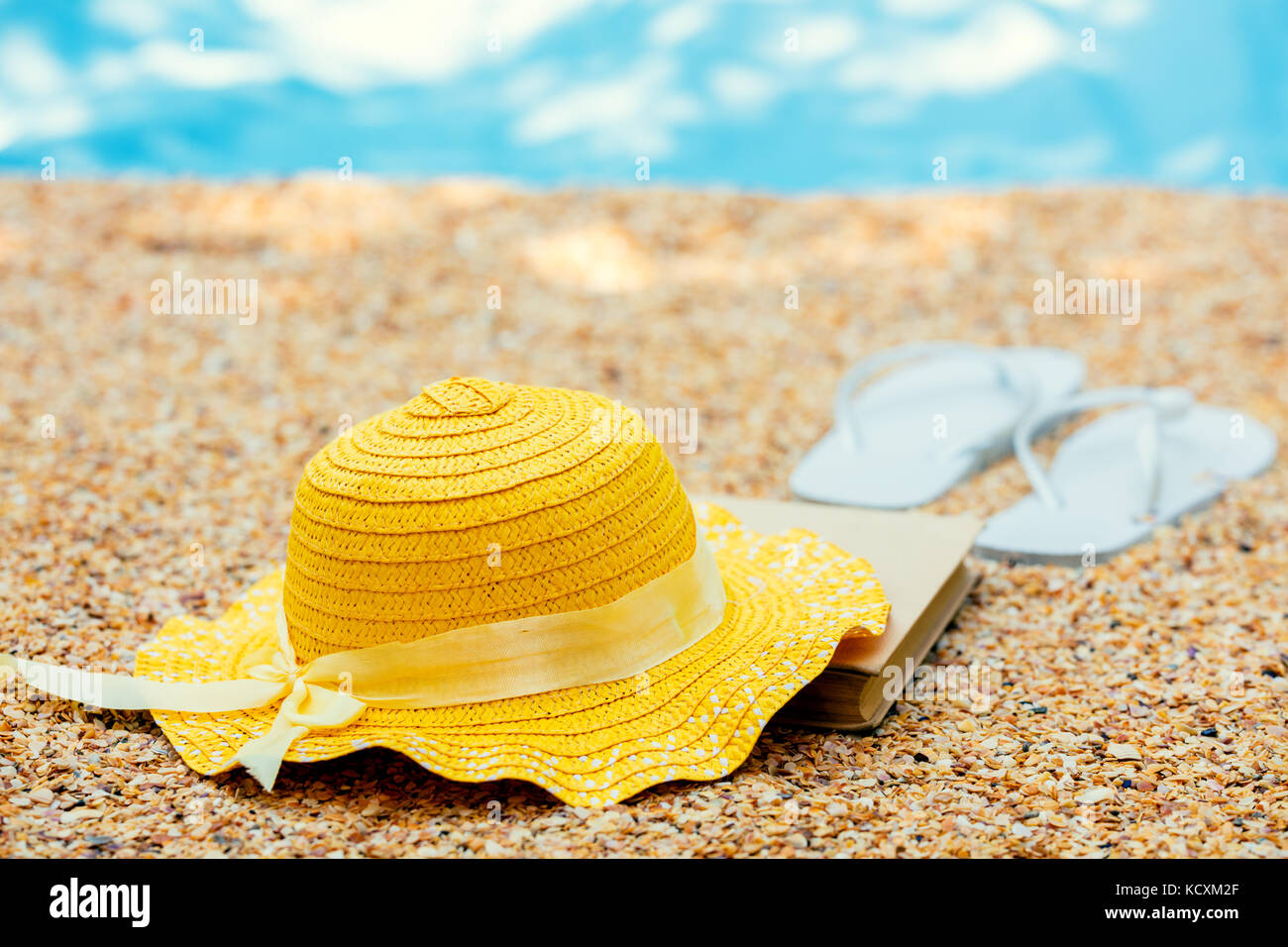 Scena di spiaggia. Sun cappello di paglia, e flip flop sandals giacente sul mare coquina conchiglie sulla spiaggia Foto Stock