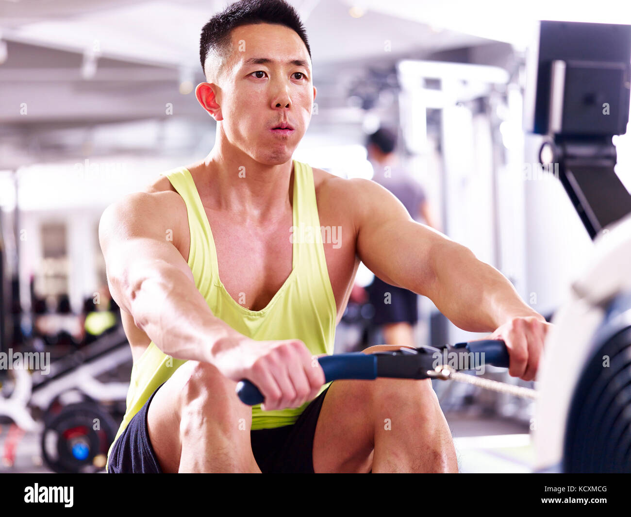 Giovani asiatici uomo muscolare che esercitano nel centro fitness con vogatore. Foto Stock