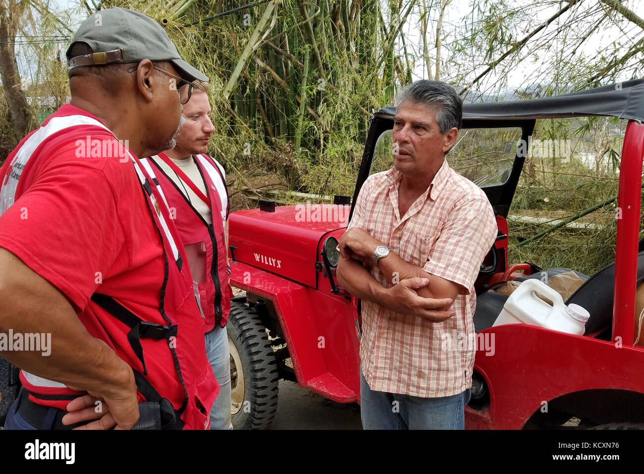 Geno Rosario e Tom Lemere, American i volontari della Croce Rossa, parlare con Juan Rivera, un agricoltore in Utuado, Puerto Rico, dopo la fornitura di lui con un telo per la sua casa il 5 ottobre 2017. Lemere, nativo di Saratoga Springs, New York, assegnato all'aria 541th ala mobilità basata sulla giunzione baseGuire-Dix Mc-Lakehurst, N.J., è parte di un team di locali, stateside e volontari internazionali che hanno consegnato la tarps, cibo, acqua e valutati i danni nella città. Il Dipartimento della Difesa, Federal Emergency Management Agency e altre organizzazioni hanno unito gli sforzi per assistere le autorità civili a Puerto Rico a p Foto Stock