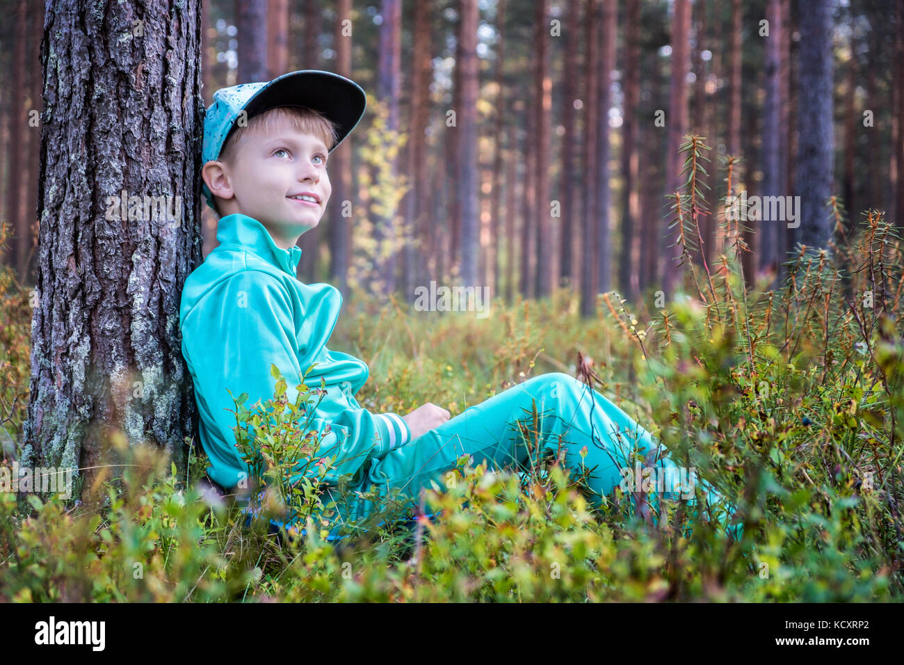 Felice giovane ragazzo seduto nella foresta e sognare Foto Stock