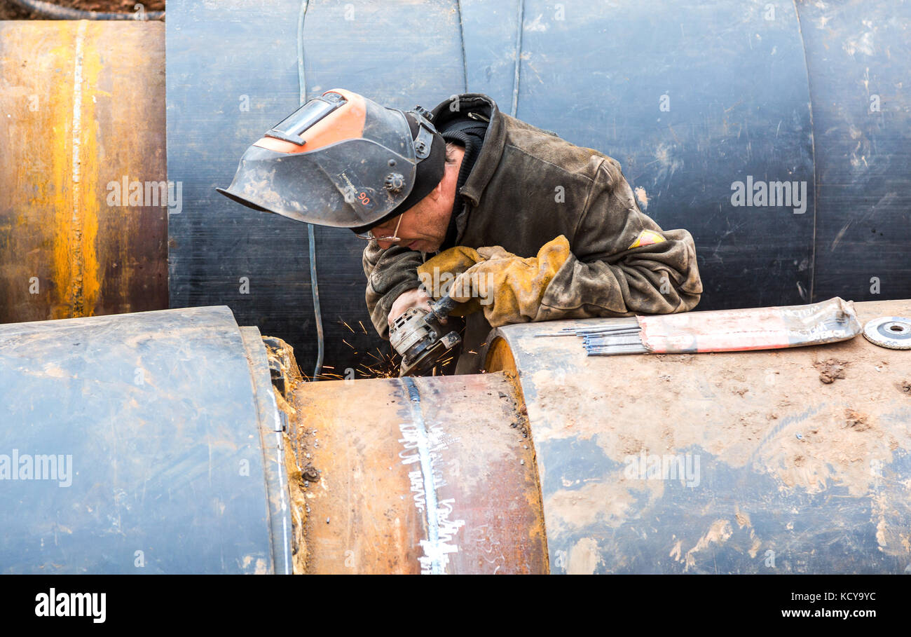 Samara, Russia - 1 ottobre 2017: Lavoratore, indossa abiti protettivi, lavora su un prodotto di tubi metallici, mola e produce scintille Foto Stock