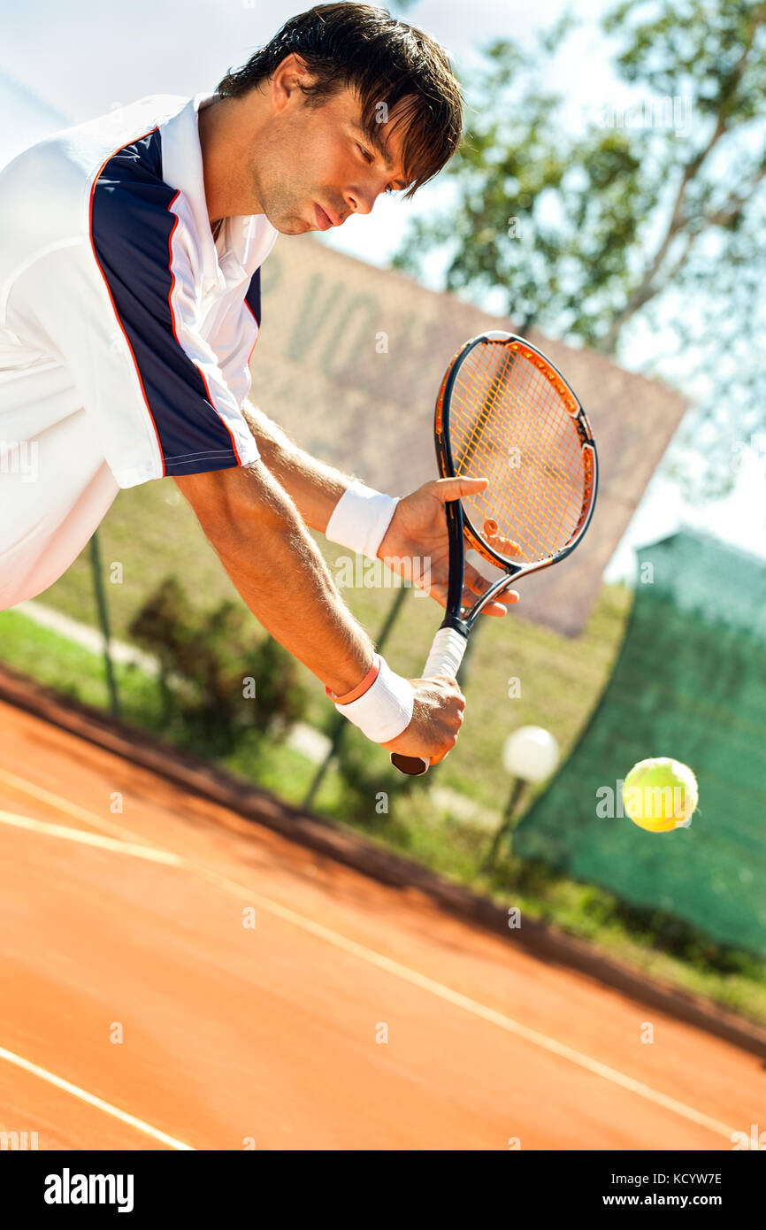 Giovane uomo giocando a tennis, colpendo la palla da tennis Foto Stock