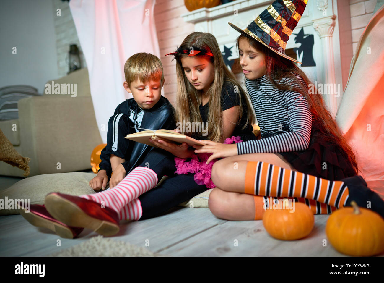 Gruppo di simpatici ragazzi indossando costumi di Halloween riuniti presso  sala decorata per le vacanze e la lettura di brevi storie di paura Foto  stock - Alamy