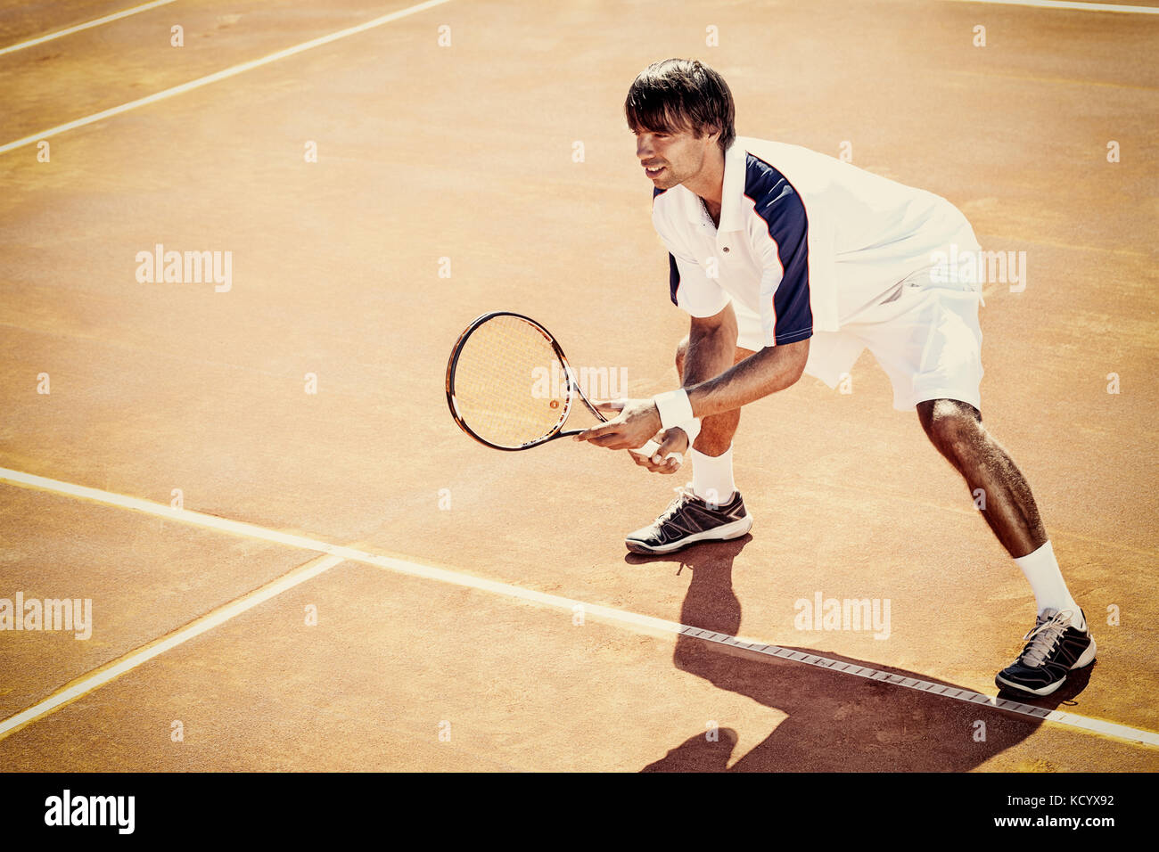 Giovane uomo a giocare a tennis all'aperto su orange campo da tennis Foto Stock