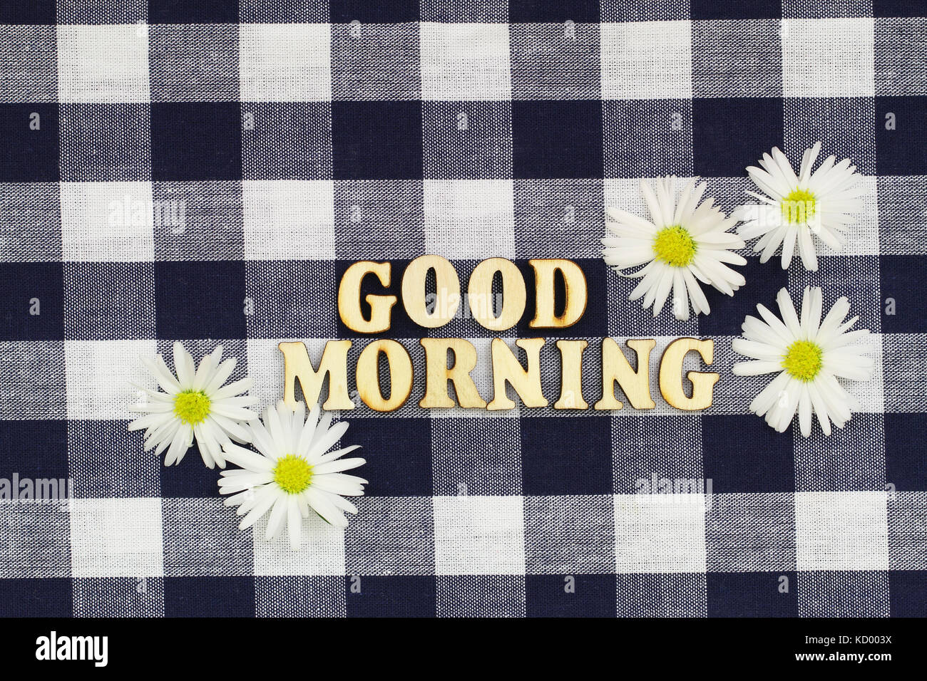 Buona mattina scritto con lettere in legno sul panno a scacchi con bianco fiori a margherita Foto Stock
