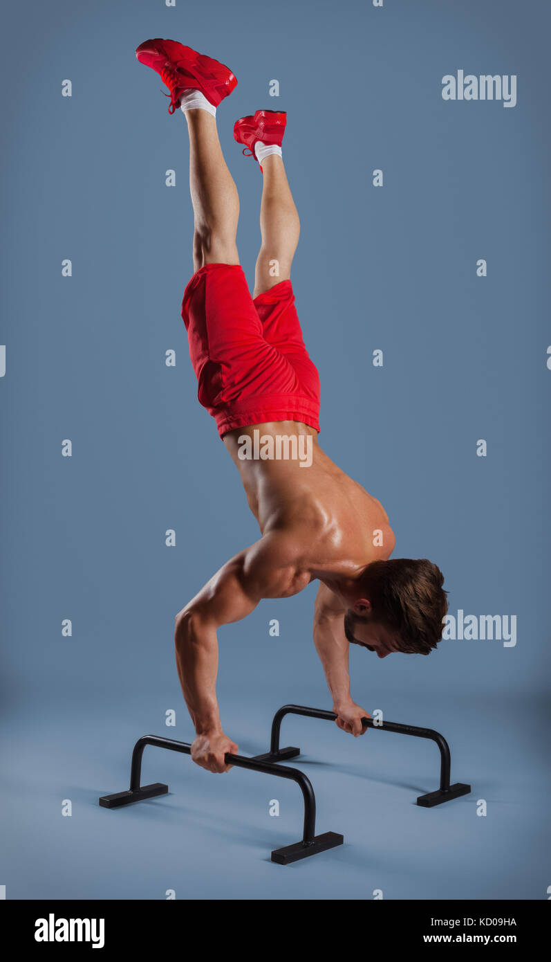 Forte atleta maschio mostra calisthenic sposta le gambe estese planche push ups sulle barre parallele, studio shot Foto Stock