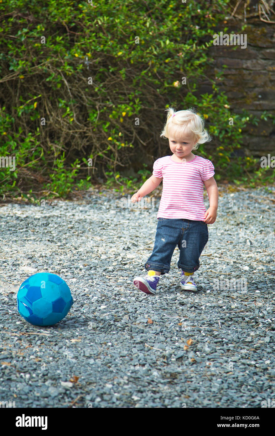 Una bambina da 2 a 3 anni di calci un pallone da calcio Foto Stock