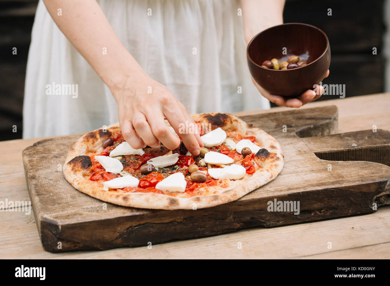 Donna mettendo le olive su pizze, metà sezione Foto Stock
