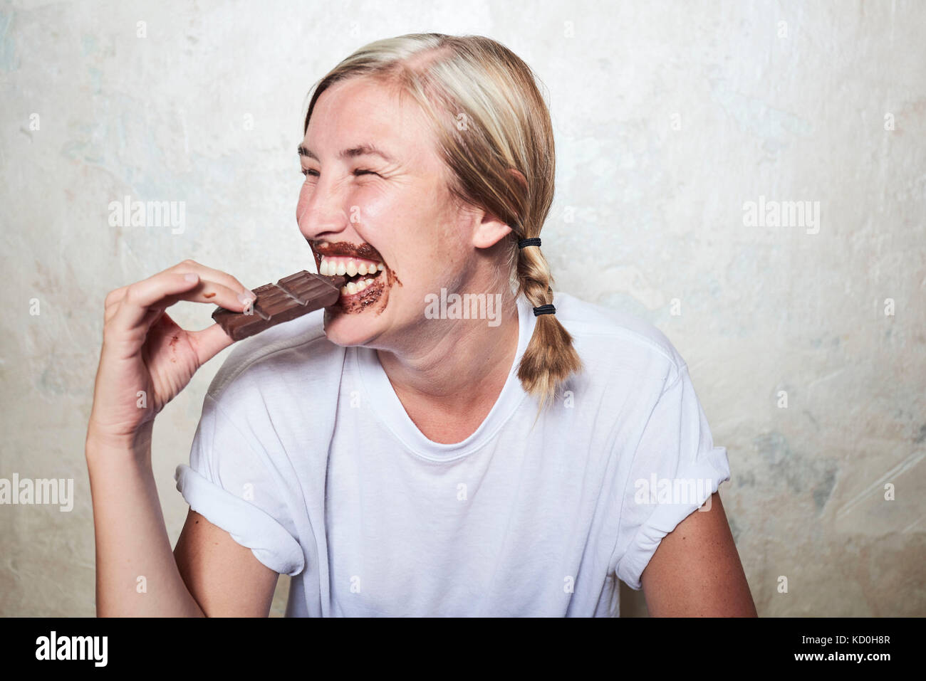 Donna di mangiare bar di cioccolato, cioccolato attorno alla bocca, ridendo Foto Stock