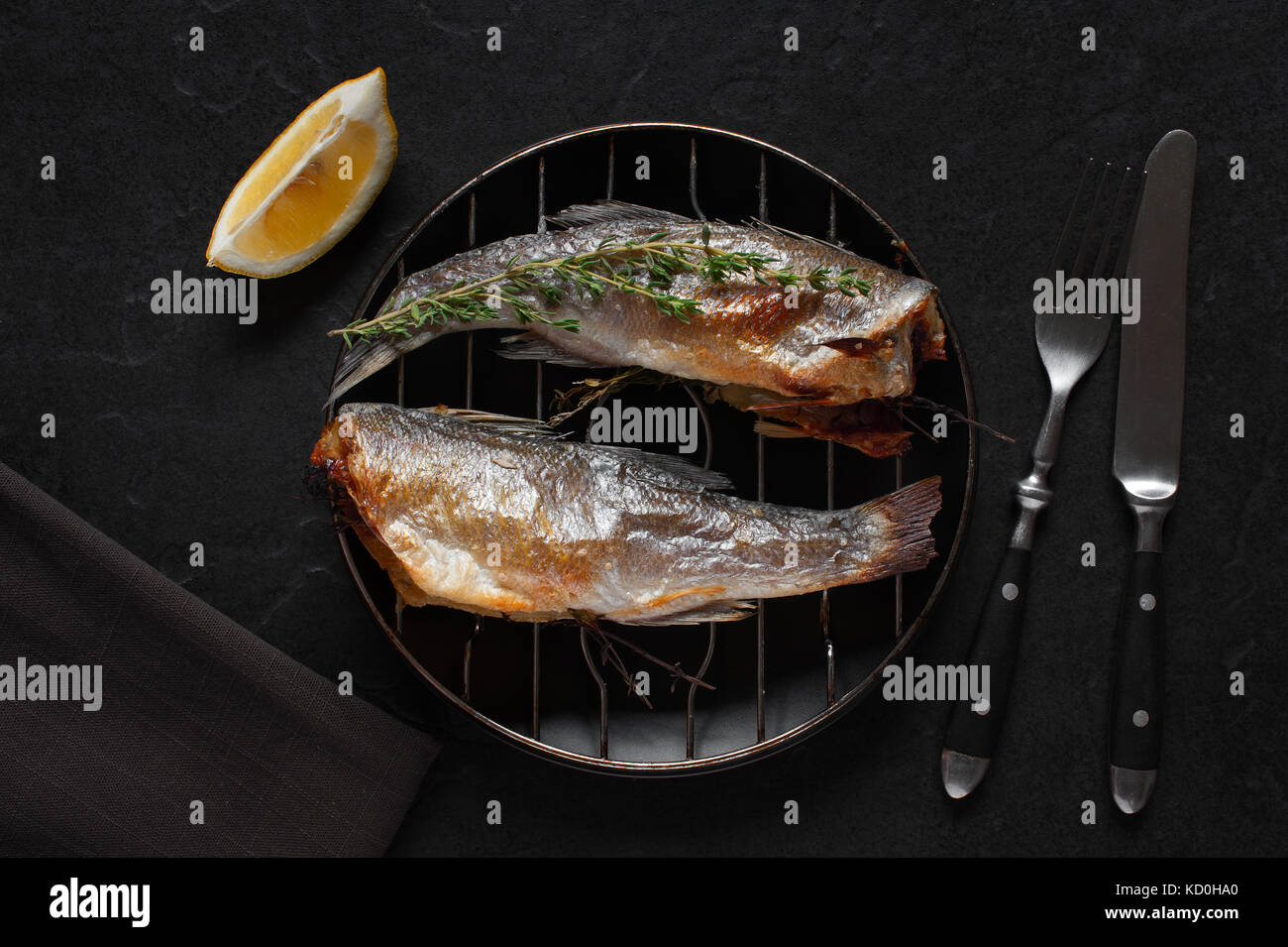 Pesce fritto con timo e limone sul nero tavolo di pietra Foto Stock