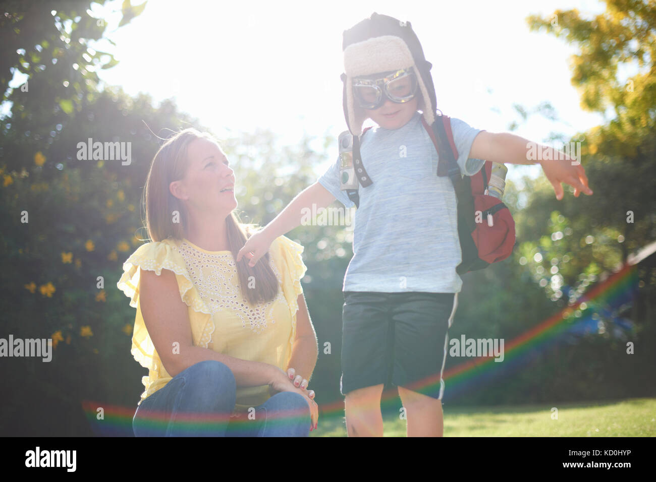 Donna matura con figlio fingendo di essere pilota con i bracci aperti nel giardino soleggiato Foto Stock