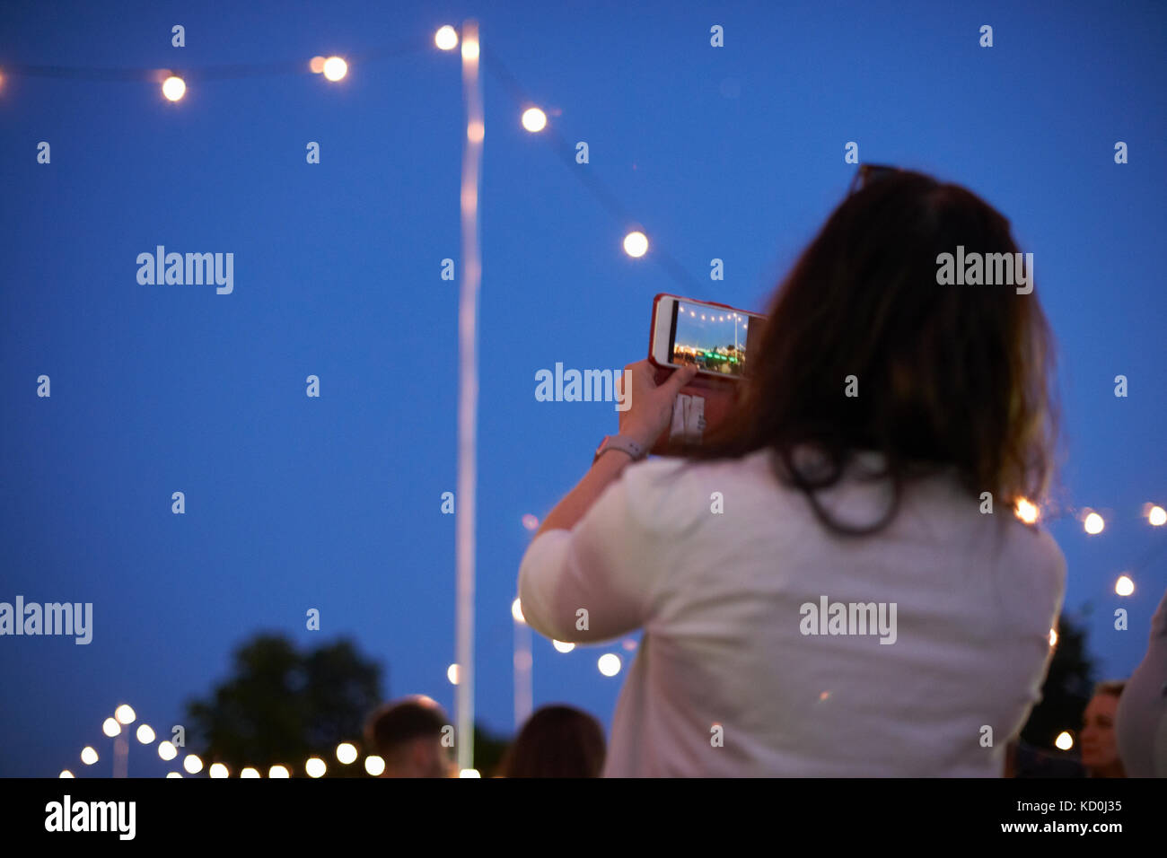 Donna matura a fotografare il cielo blu e luci al mercato notturno festival di park, london, Regno Unito Foto Stock