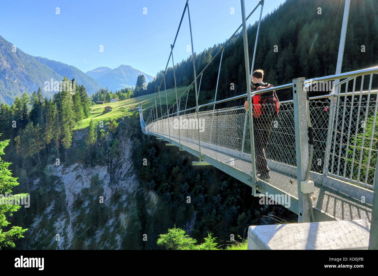 HOLZGAU, AUSTRIA 18 giugno 2017: Un uomo con uno zaino cammina su un ponte sospeso a Holzgau, Austria. Il villaggio di Holzgau è famoso per l’Austria Foto Stock