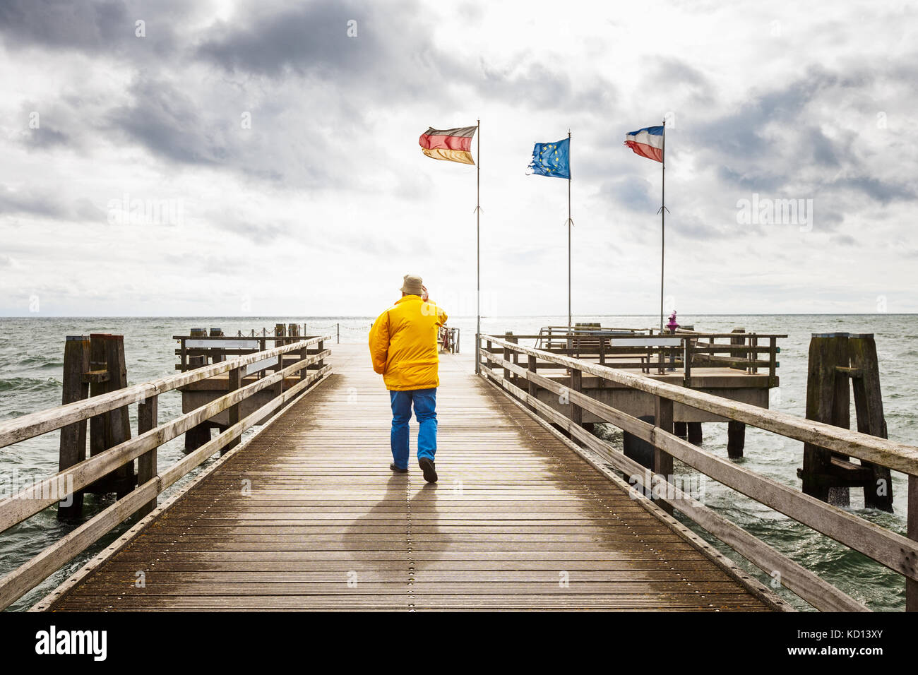 Senior uomo a camminare sulla spiaggia molo di legno. tarda estate del paesaggio con il vento e il cielo nuvoloso. vacanza sfondo. mar baltico, Germania, viaggi destin Foto Stock