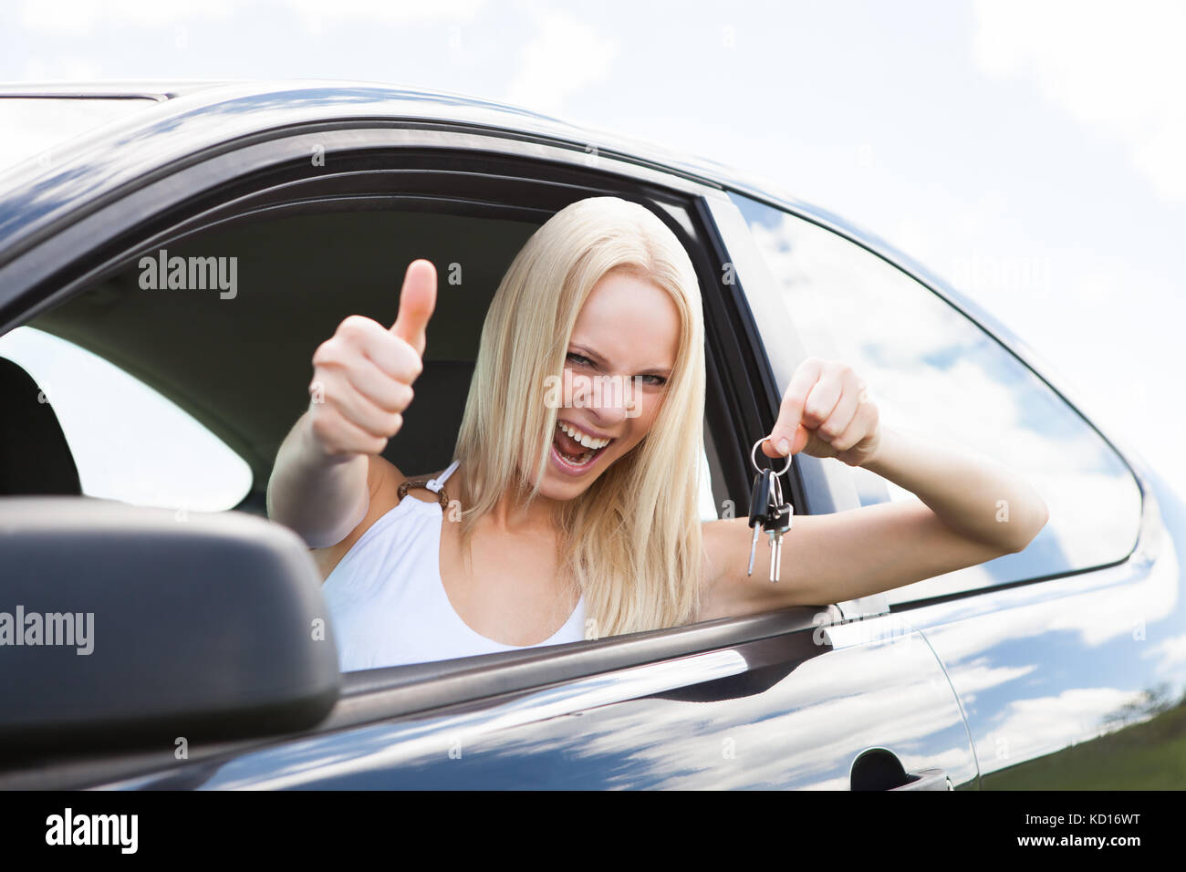 Donna felice in una vettura che mostra una chiave e gesticolando pollice in alto Foto Stock
