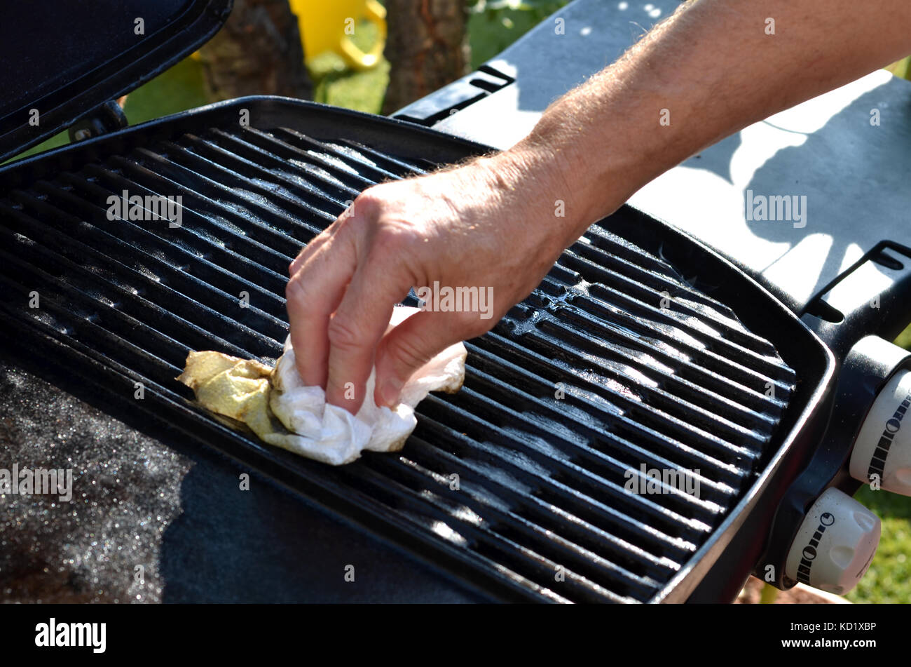 Primo piano sulla mano dell'uomo che spruzza olio sulla griglia a gas del  barbecue all'aperto nel cortile