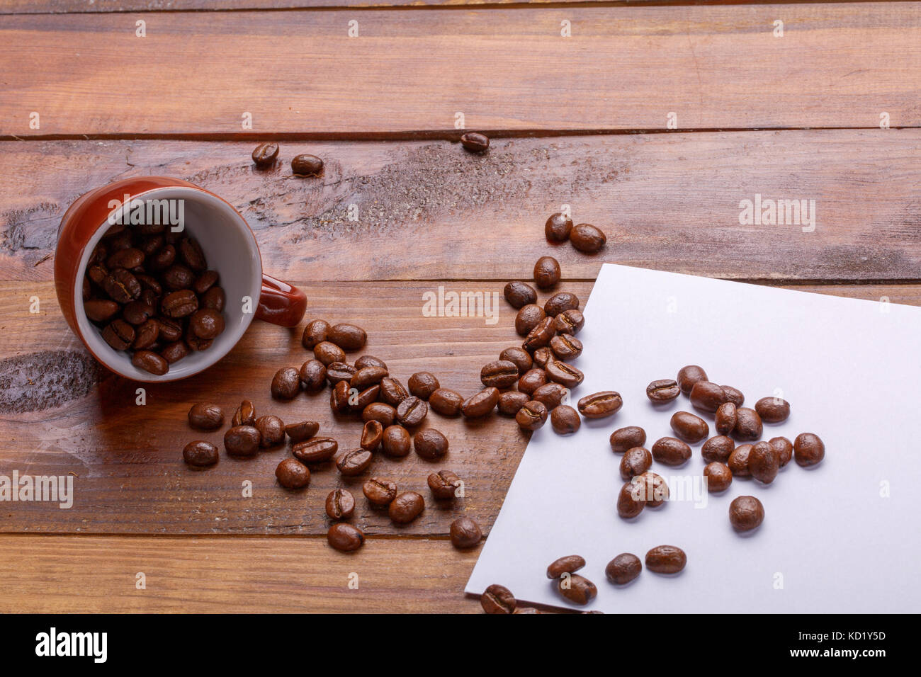 Ottenere abbastanza sonno da una tazza di caffè granella. caffè in chicchi di ottenere al di fuori del bicchiere su carta e broun sfondo di legno Foto Stock