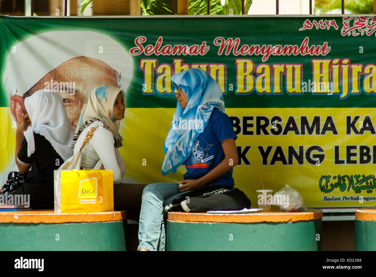 In corrispondenza di un Autobus Alloggio in Kota Bharu, stato di Kelantan, Malay le donne musulmane attendere accanto a un cartellone per celebrare l'annuale Hijra o pellegrinaggio alla Mecca. Foto Stock