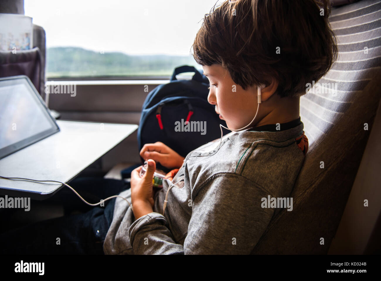 Ragazzo che viaggiano in treno, utilizzando digitale compressa, indossa gli auricolari Foto Stock