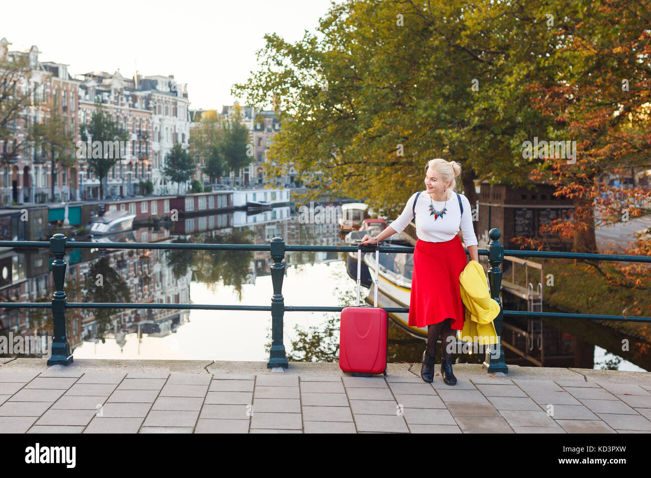 La donna con la valigia è in appoggio sul ponte della città di Amsterdam in autunno Foto Stock