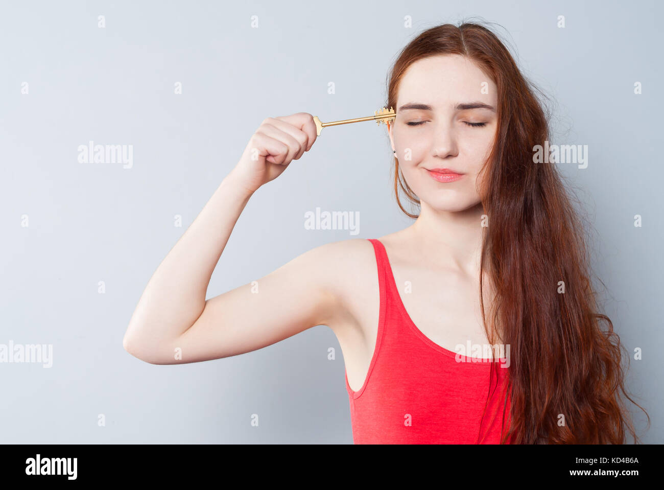 Una giovane donna carina con gli occhi chiusi detiene una grande chiave accanto alla sua testa, tentando di aprire la sua mente o testa. Il concetto di creatività, ampiezza di pensare Foto Stock