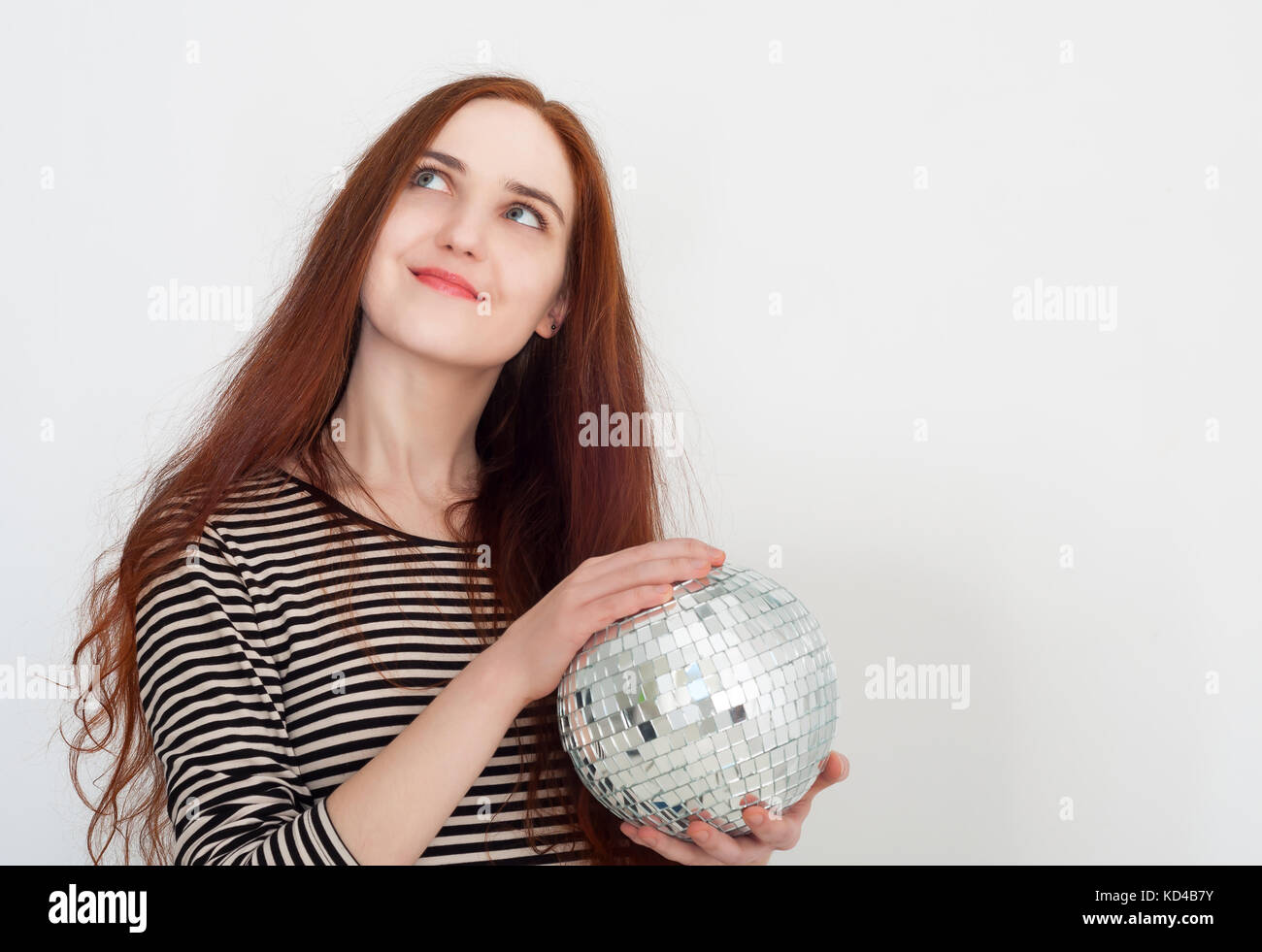 Bellissimi i Capelli rossi ragazza con uno specchio palla da discoteca nelle sue mani e sorridendo. Preparazione per una festa e le vacanze. Foto Stock