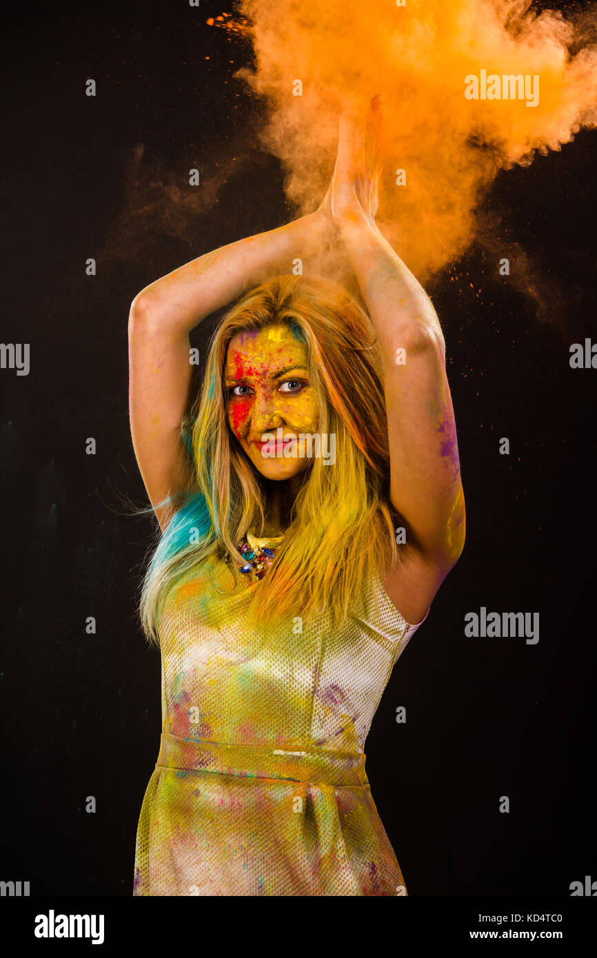 Bella giovane donna con polvere colorata su backgrond scuro Foto Stock