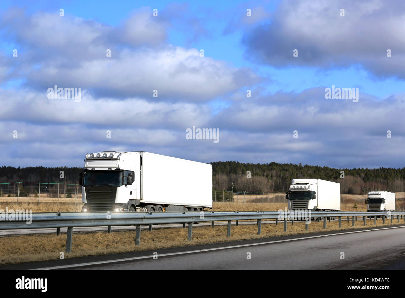 Tre bianchi semi rimorchio camion Cargo plotone sulla freeway a molla con il cielo blu e nuvole sfondo. copia superiore dello spazio dell'immagine. Foto Stock