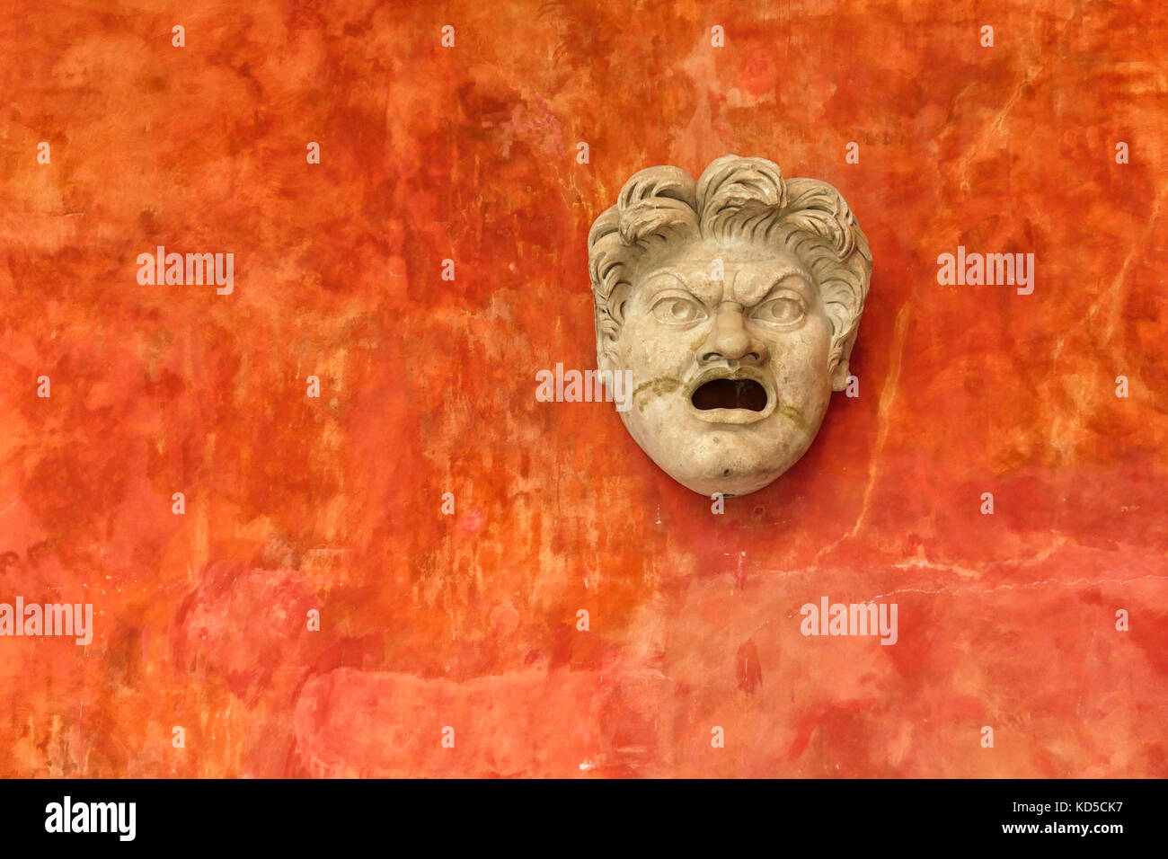 Faccia di pietra di angry man contro un arancio brillante parete. antica testa romana nel museo Glyptotek di Copenhagen, Danimarca Foto Stock