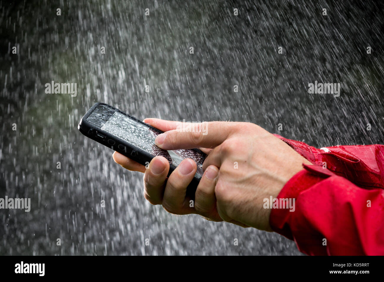 Un uomo con un telefono cellulare in una custodia impermeabile al di fuori sotto la pioggia Foto Stock