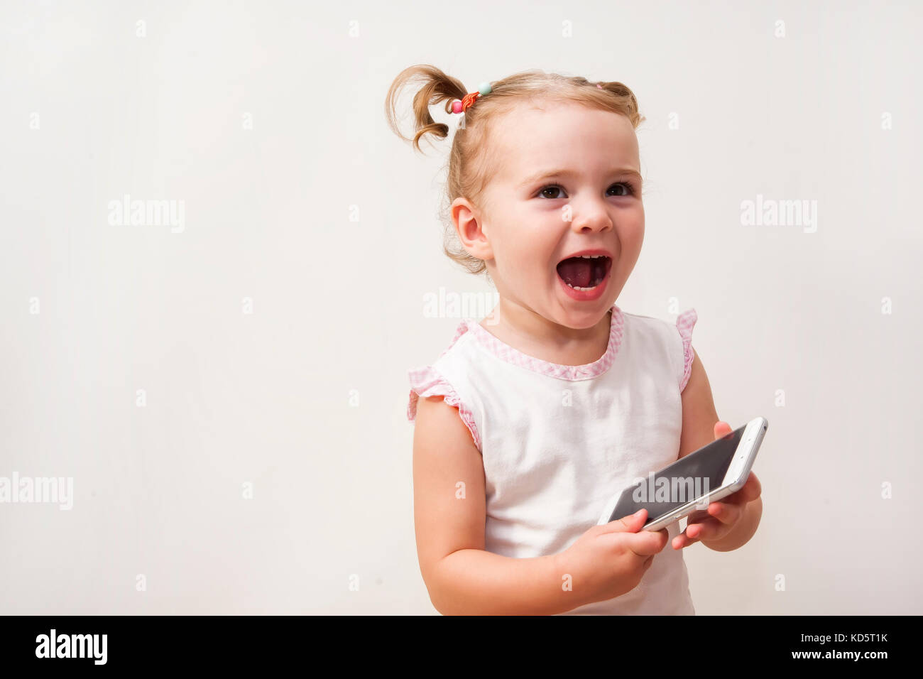 Bambina gioca con un telefono cellulare isolato su uno sfondo bianco Foto Stock