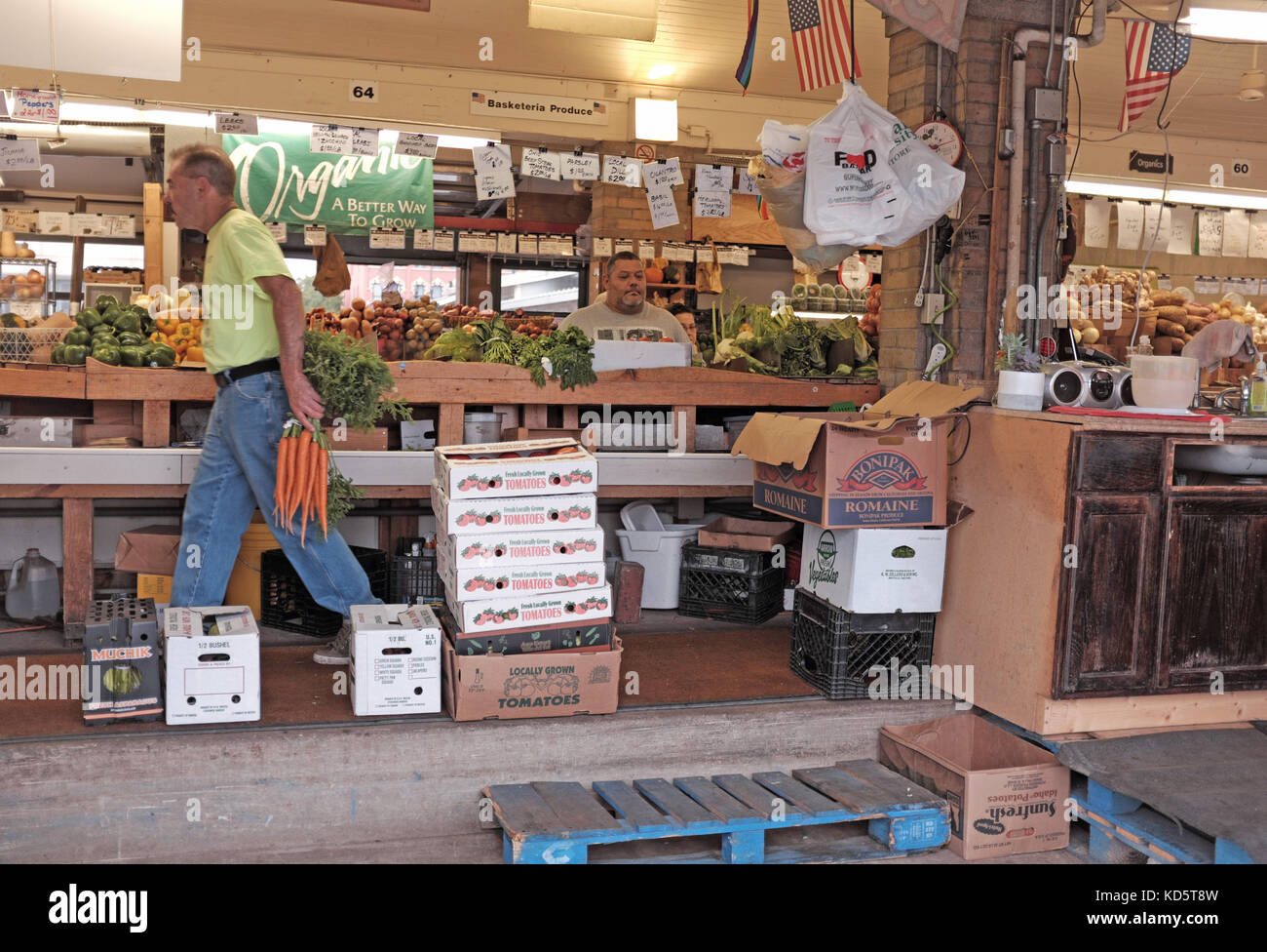 Il venditore di prodotti del West Side Market di Cleveland trasporta carote per pesarle mentre un cliente attende al banco all'interno di questo edificio storico. Foto Stock