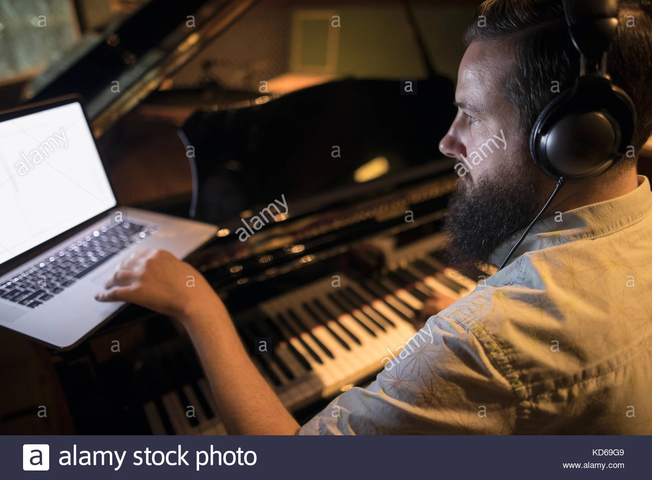 Pianista maschile che suona pianoforte grande, scrive musica al portatile in studio di registrazione Foto Stock