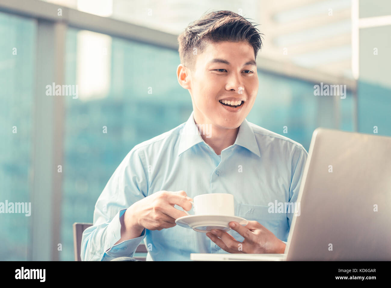 Imprenditore cinese avente caffè al suo laptop seduto davanti Foto Stock