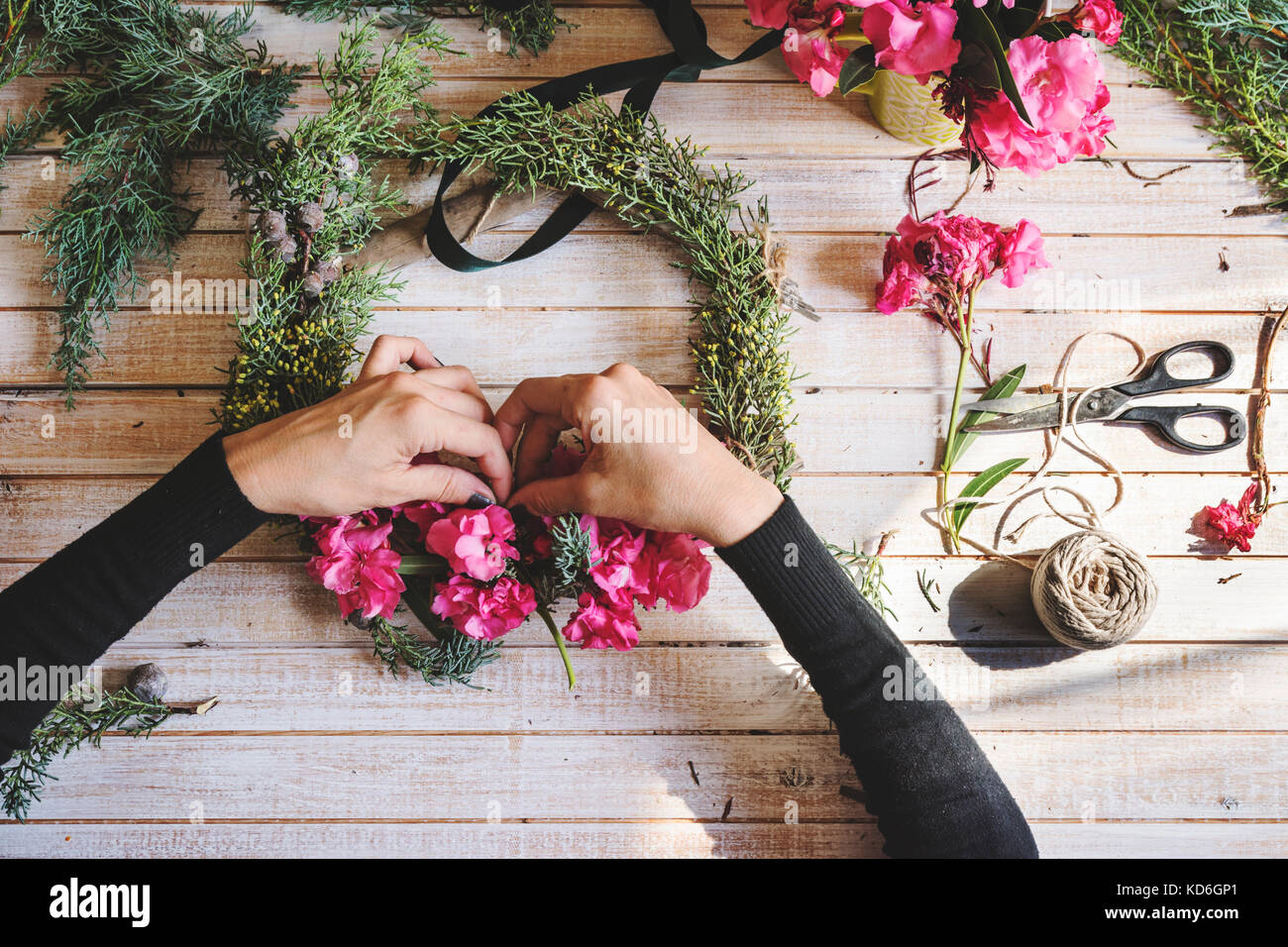 Fioraio al lavoro: creazione di una ghirlanda di legno con rami di pino e fiori di colore rosa e circondato dalle arti e mestieri. Tettuccio Foto Stock