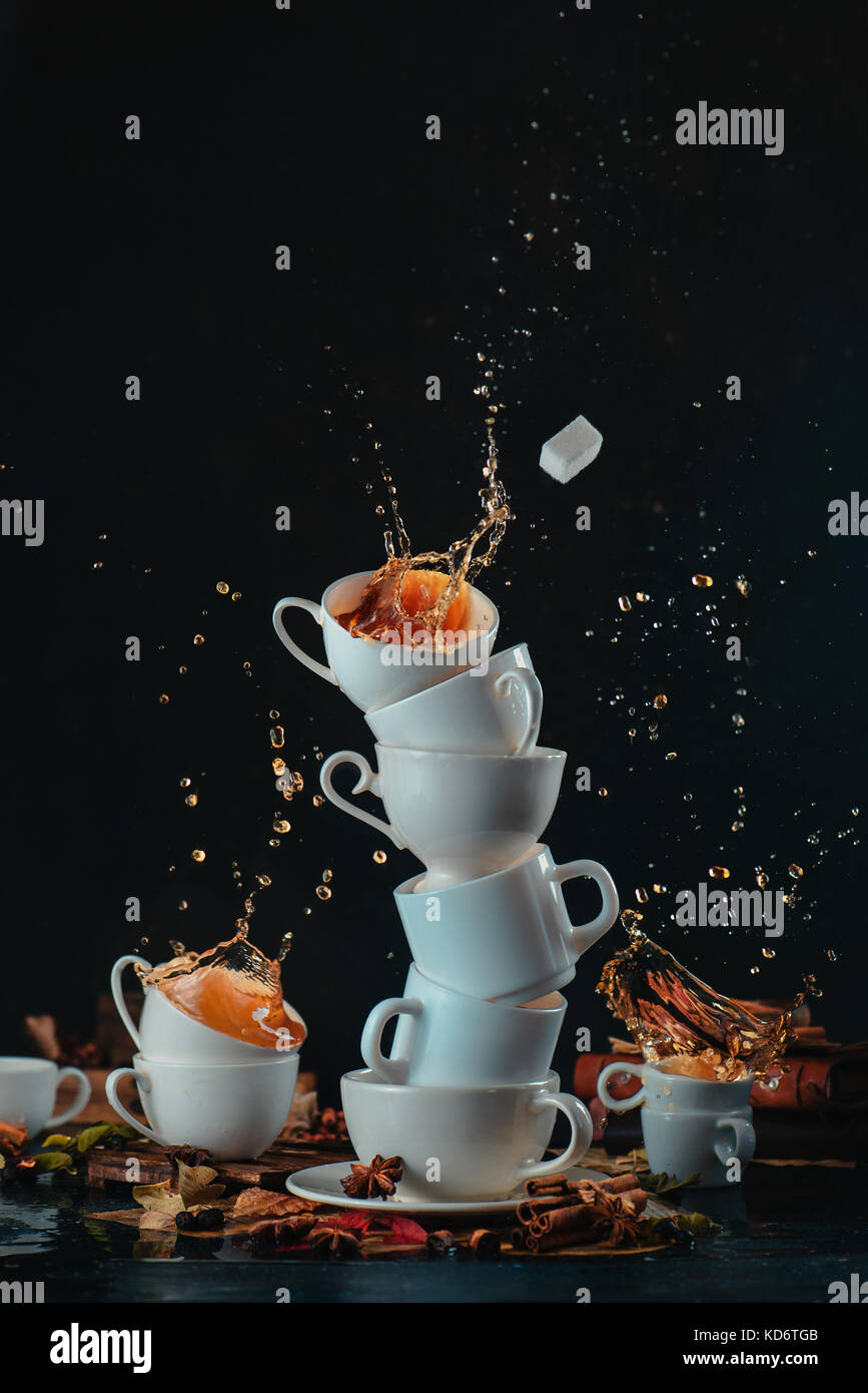 Pila di bianco tazze di caffè con gli spruzzi di dinamica e caffè scende su uno sfondo scuro. Cucina pasticcio e mad tea time concetto. azione fotografia di cibo Foto Stock