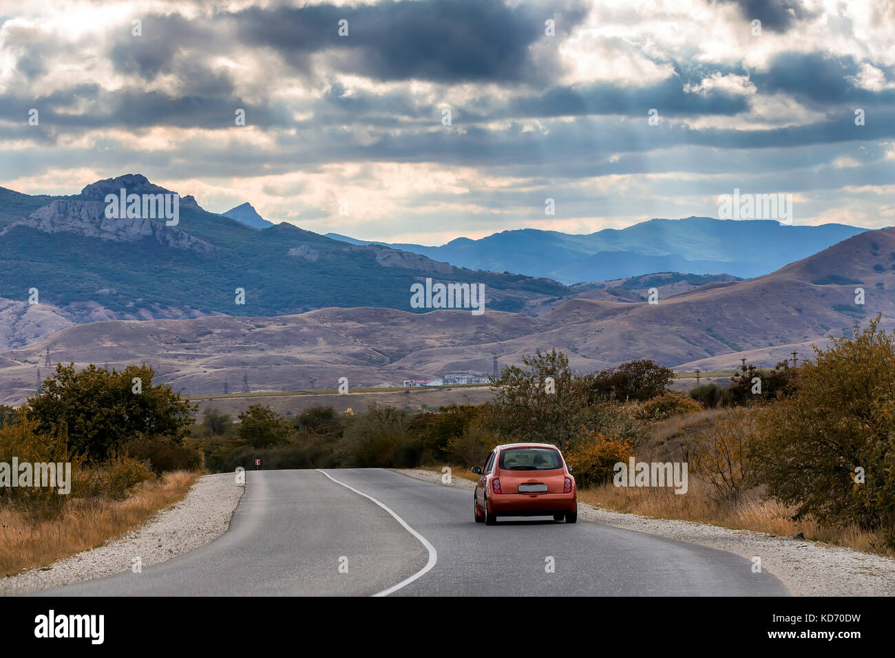 La rossa vettura viaggia lungo l'autostrada, attorno a un bel paesaggio. bluastro montagna tonante sotto il cielo coperto di nuvole Foto Stock