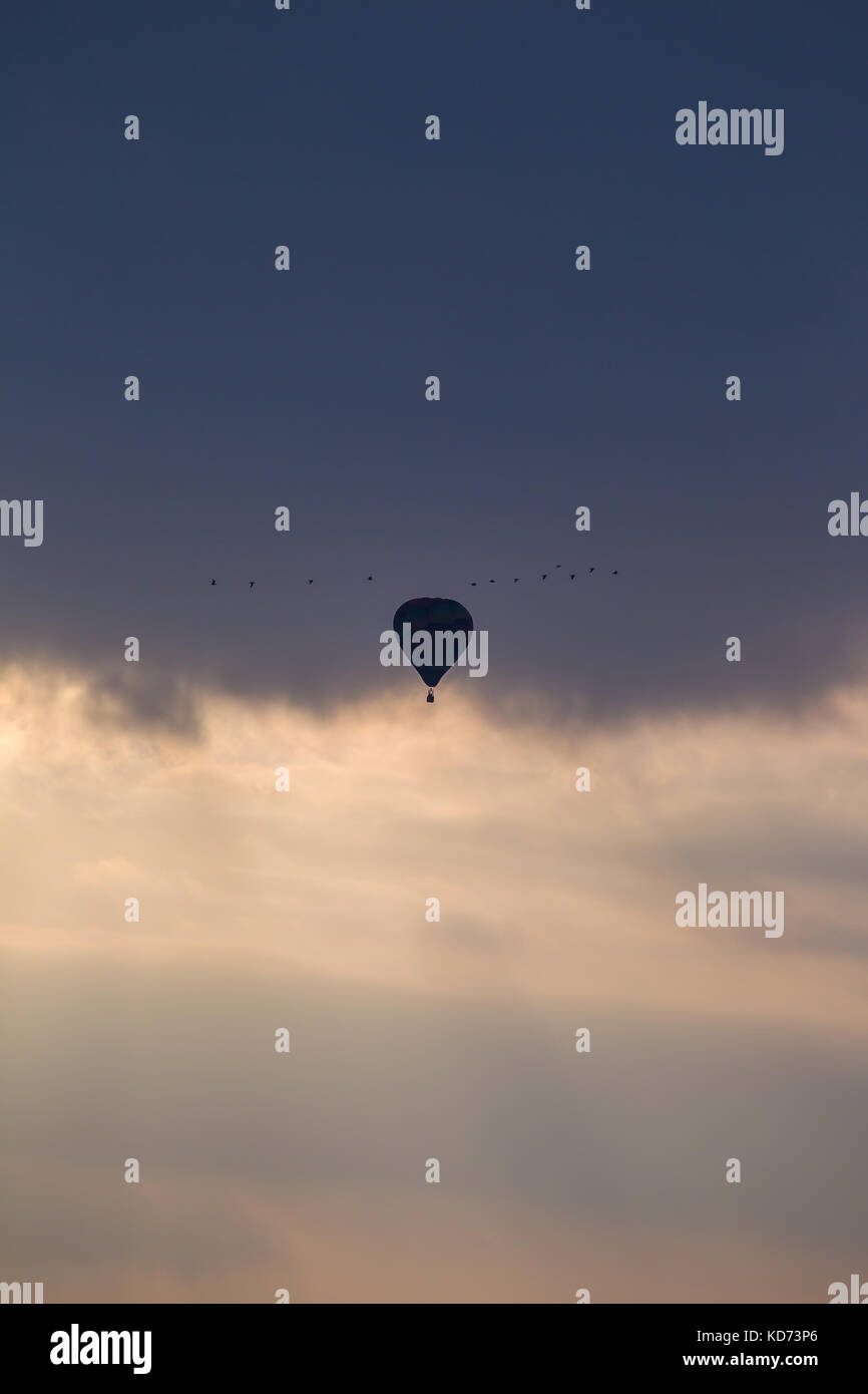 Un palloncino solitario prende il volo nel cielo di sera, passando ad alta tra le nuvole. Luce della Sera condizioni creano silhouette effetto sul palloncino. Serenità. Foto Stock
