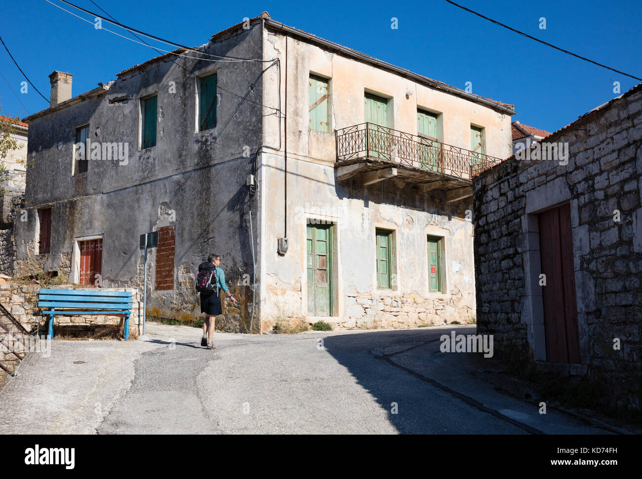 Una femmina di escursionisti a piedi passato case abbandonate lungo una ripida strada nel villaggio di Kioni su Itaca nelle isole greche ioniche Foto Stock