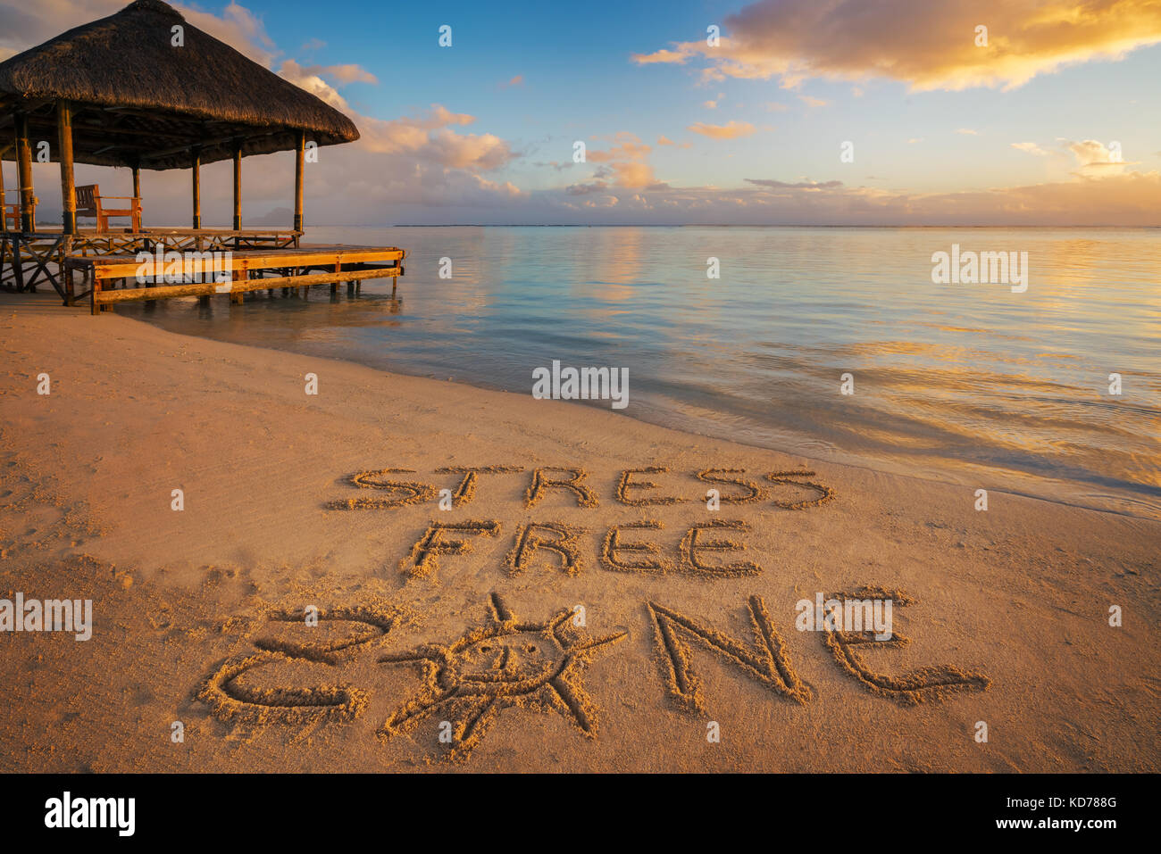Primo piano scritto nella sabbia "stress free zone' al tramonto in isola Maurizio con pontile sul lato sinistro. Foto Stock