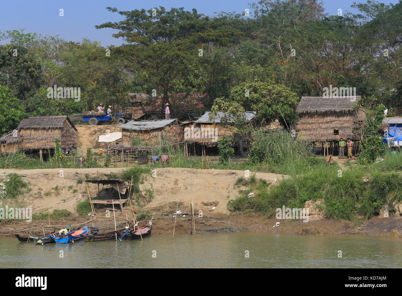 Un piccolo camion che trasporta pali di legno passa attraverso un villaggio sul fiume Irrawaddy in Myanmar (Birmania). Una piattaforma sopraelevata è accanto al fiume. Foto Stock