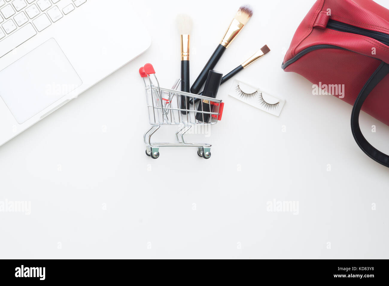 Elementi di bellezza e cosmetici nel carrello con computer portatile su sfondo bianco, shopping online Foto Stock