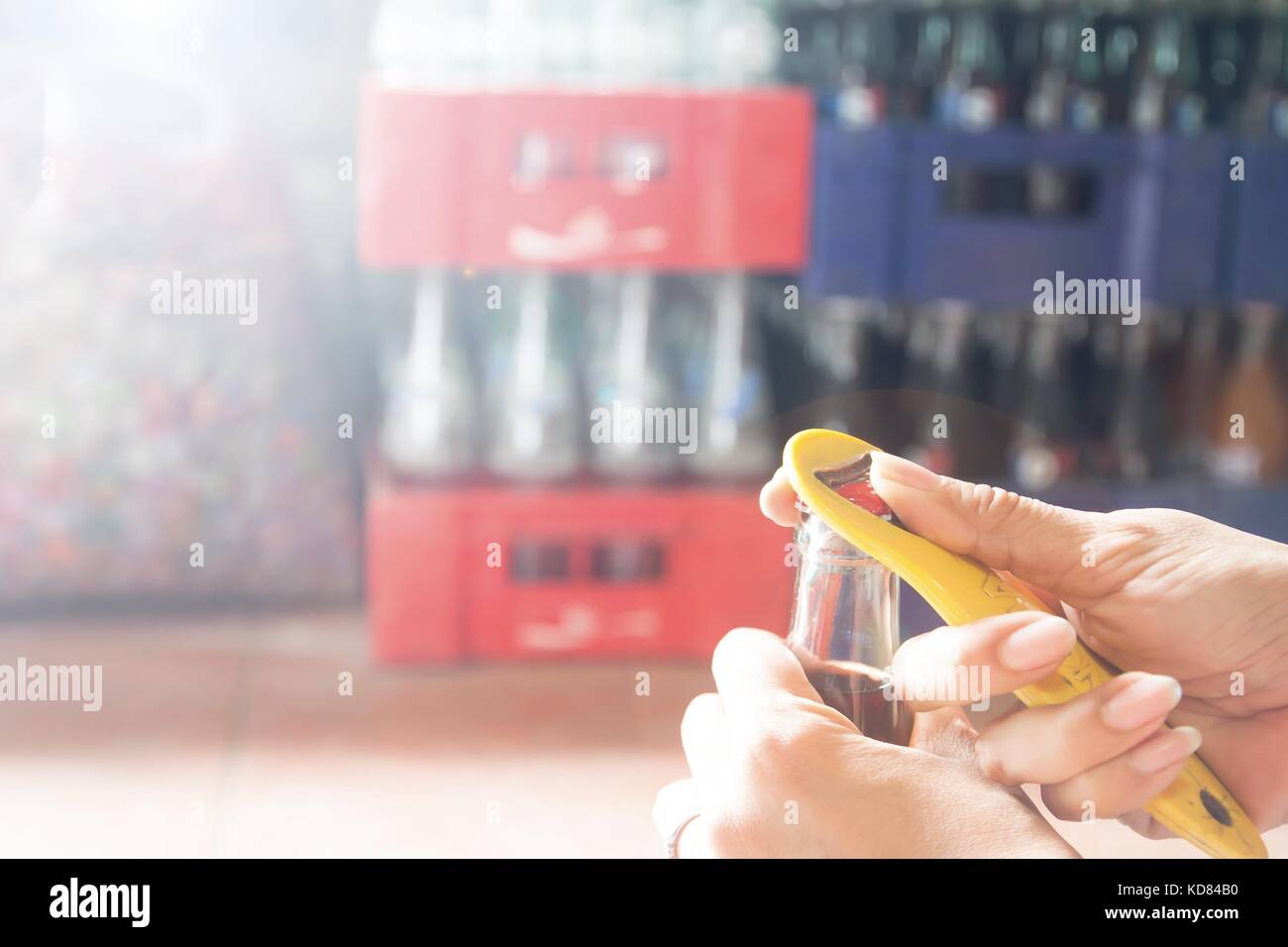 Donna mani aprendo una bottiglia di coca cola con soft drink di casse in background Foto Stock