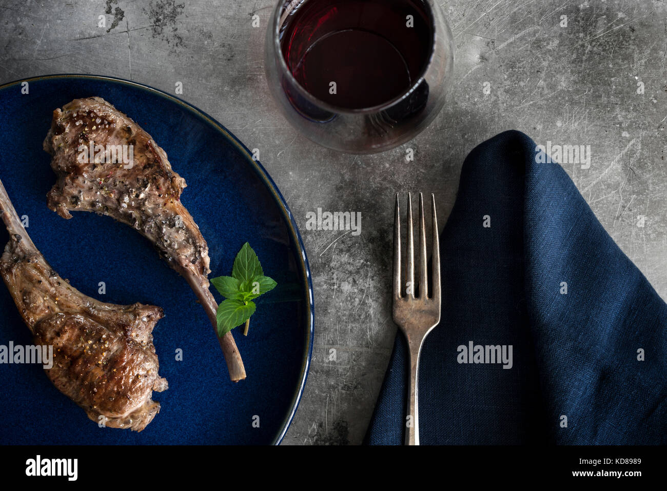 Lecca-lecca arrosto costolette di agnello su piastra blu. Impostazione  tabella con marina biancheria, vino rosso e rustico della superficie  metallica Foto stock - Alamy