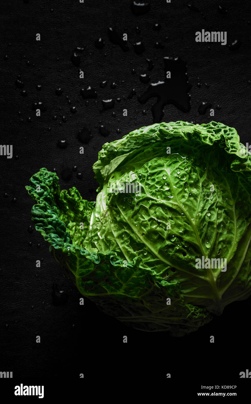 Un nuovo raccolto di testa vibrante cavolo verde con goccioline di acqua su di una superficie scura. Foto Stock