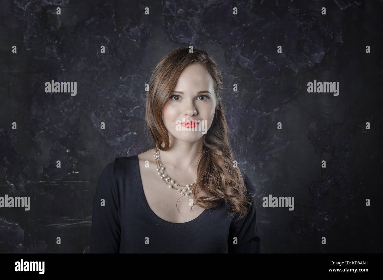 Femmina in un buon umore e un sorriso. noir film di stile donna in abiti eleganti e collana in piedi di fronte alla telecamera. ragazza ha una lunga capigliatura scura in posa con Foto Stock